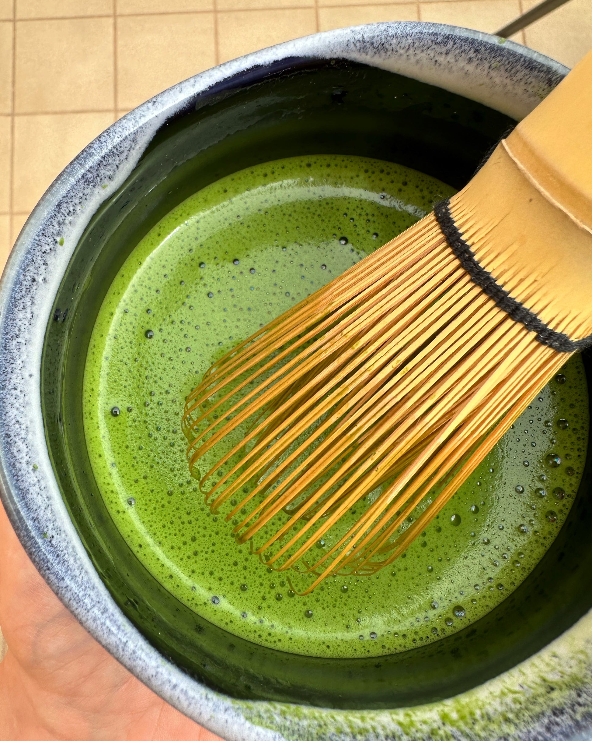 The organic ceremonial grade matcha powder mixed with water and a chased/bamboo whisk