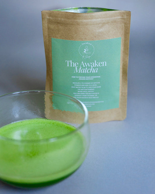Glass of green matcha tea with a package labeled 'The Awaken Matcha' on a gray background