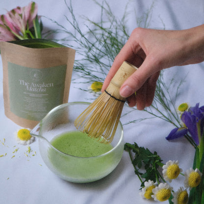 first flush matcha whisked in a glass chawan with a chasen and flowers